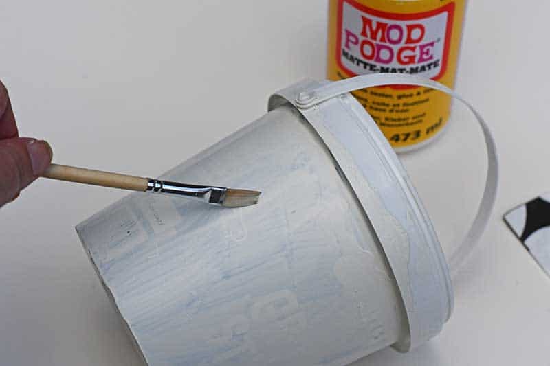 applying Mod Podge to hanging storage bucket.