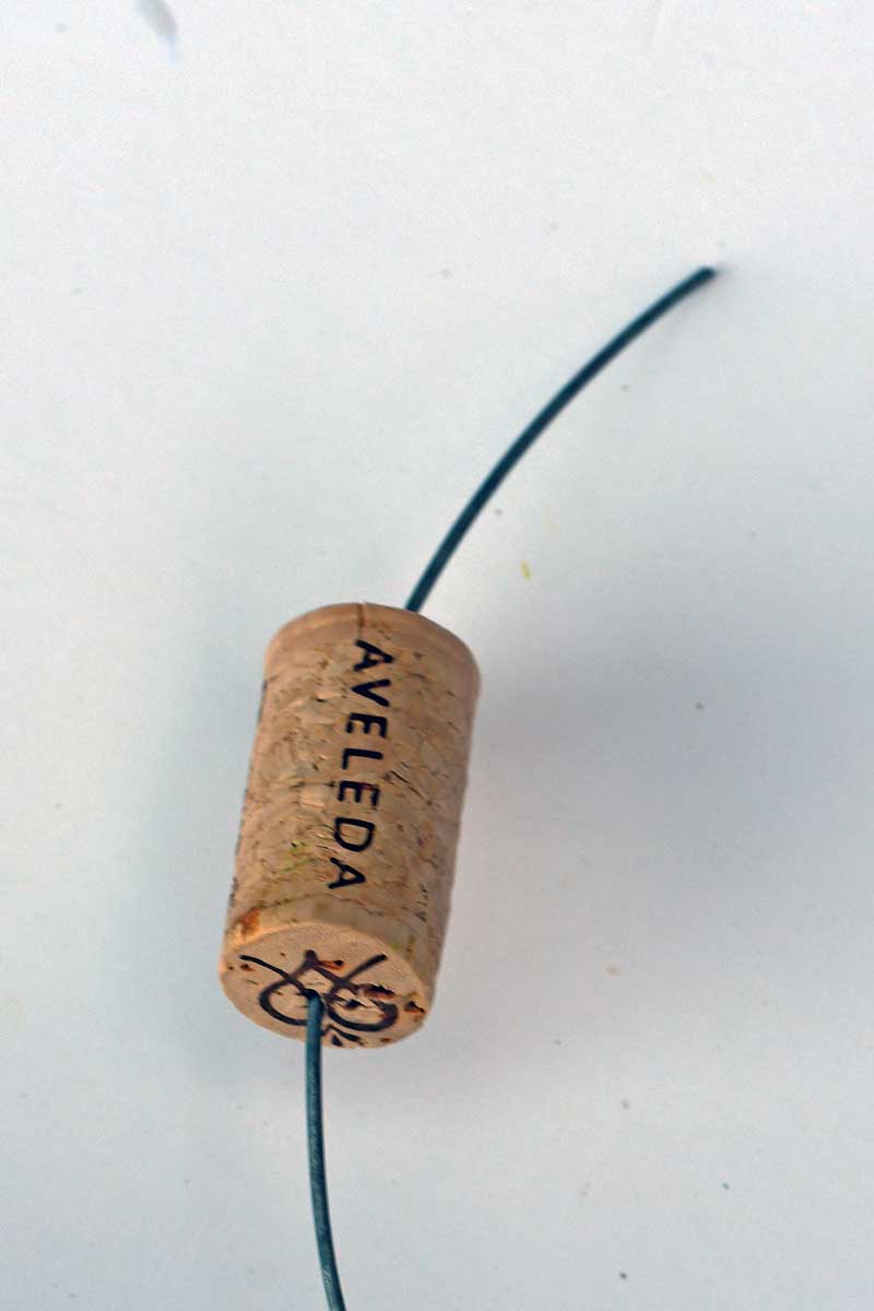 Threading wire through wine cork to make an upcycled bucket handle.