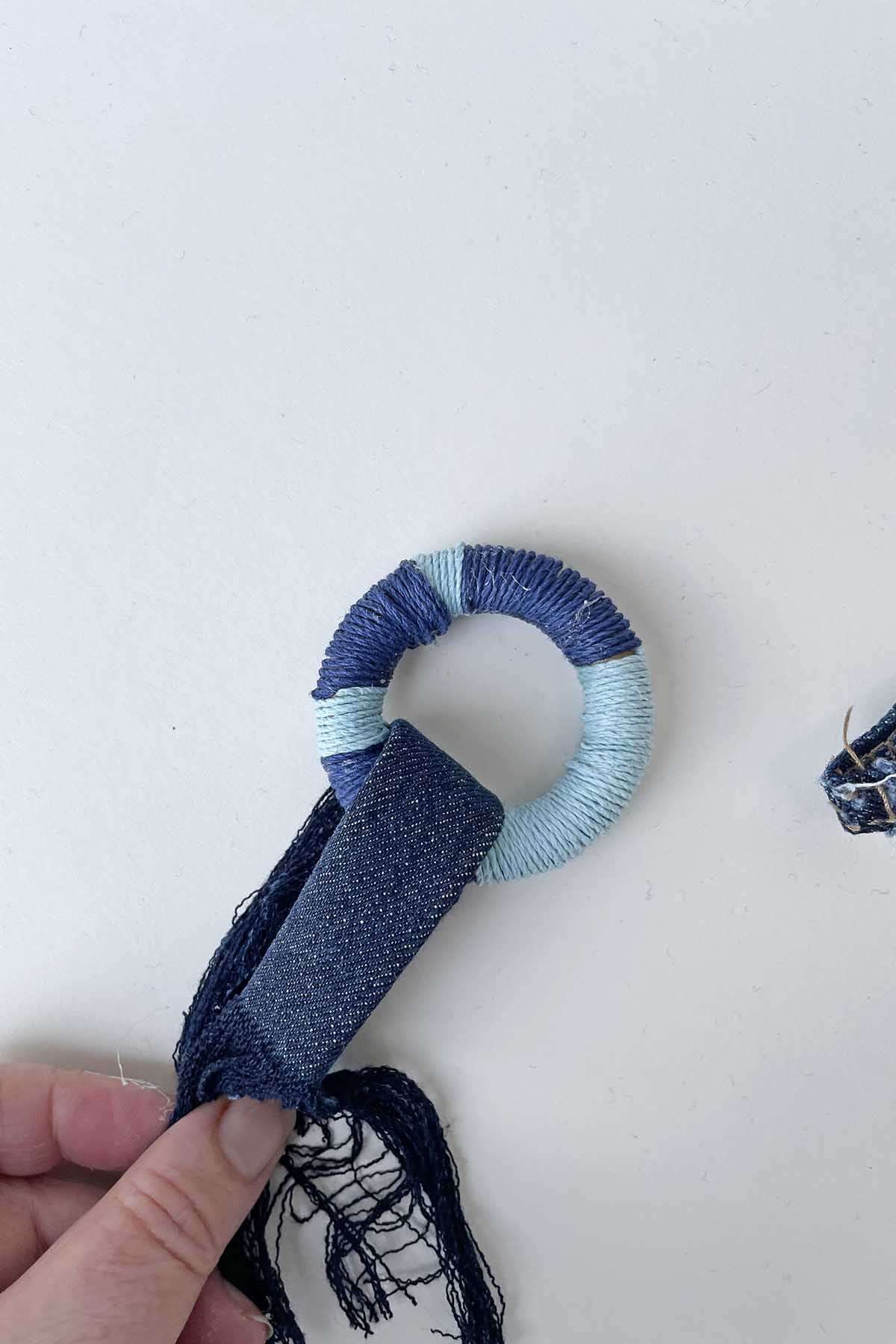 Folding the denim tassel over the wooden ring