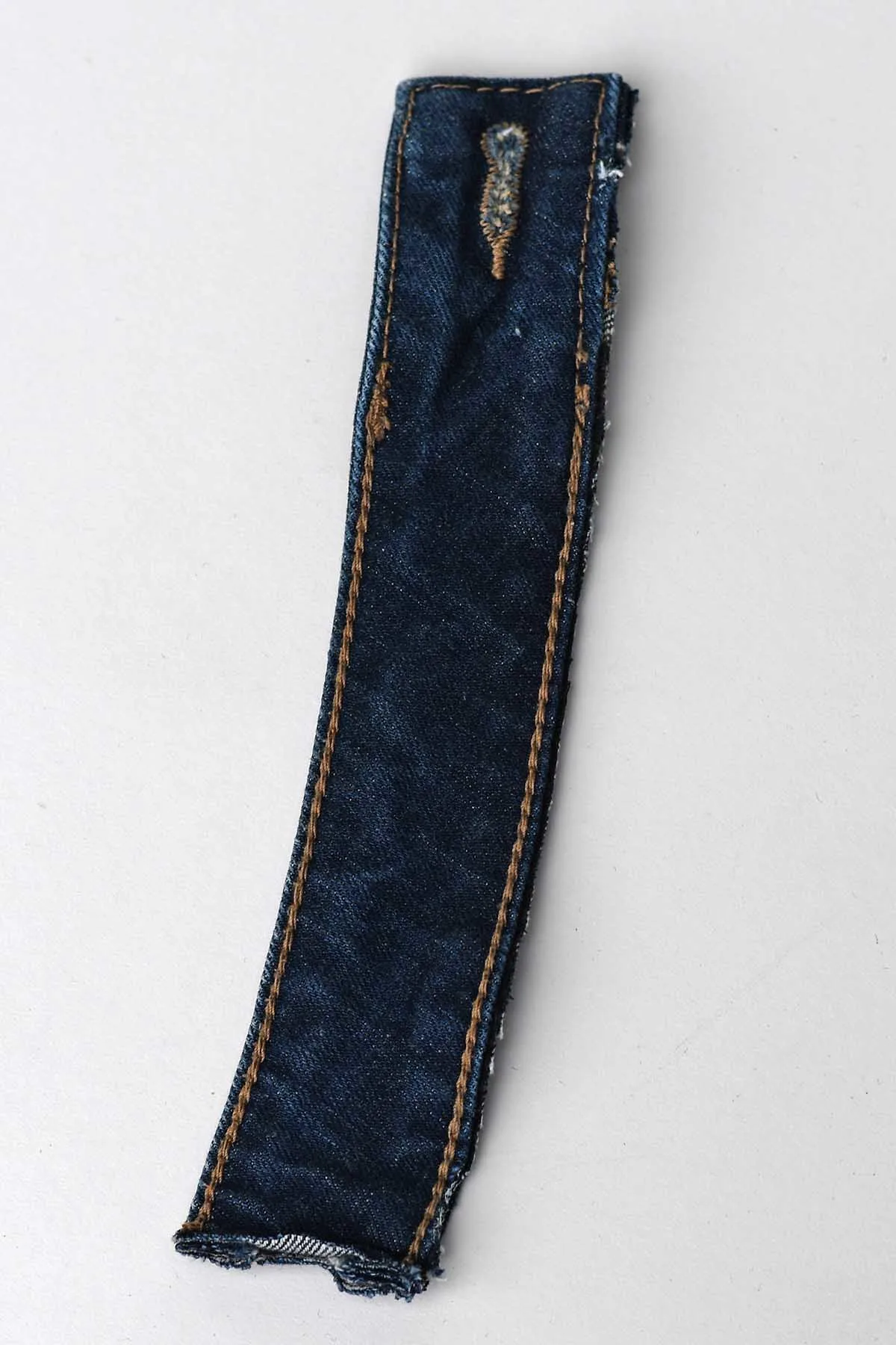 An 8" long cut piece of jeans waistband with button hole