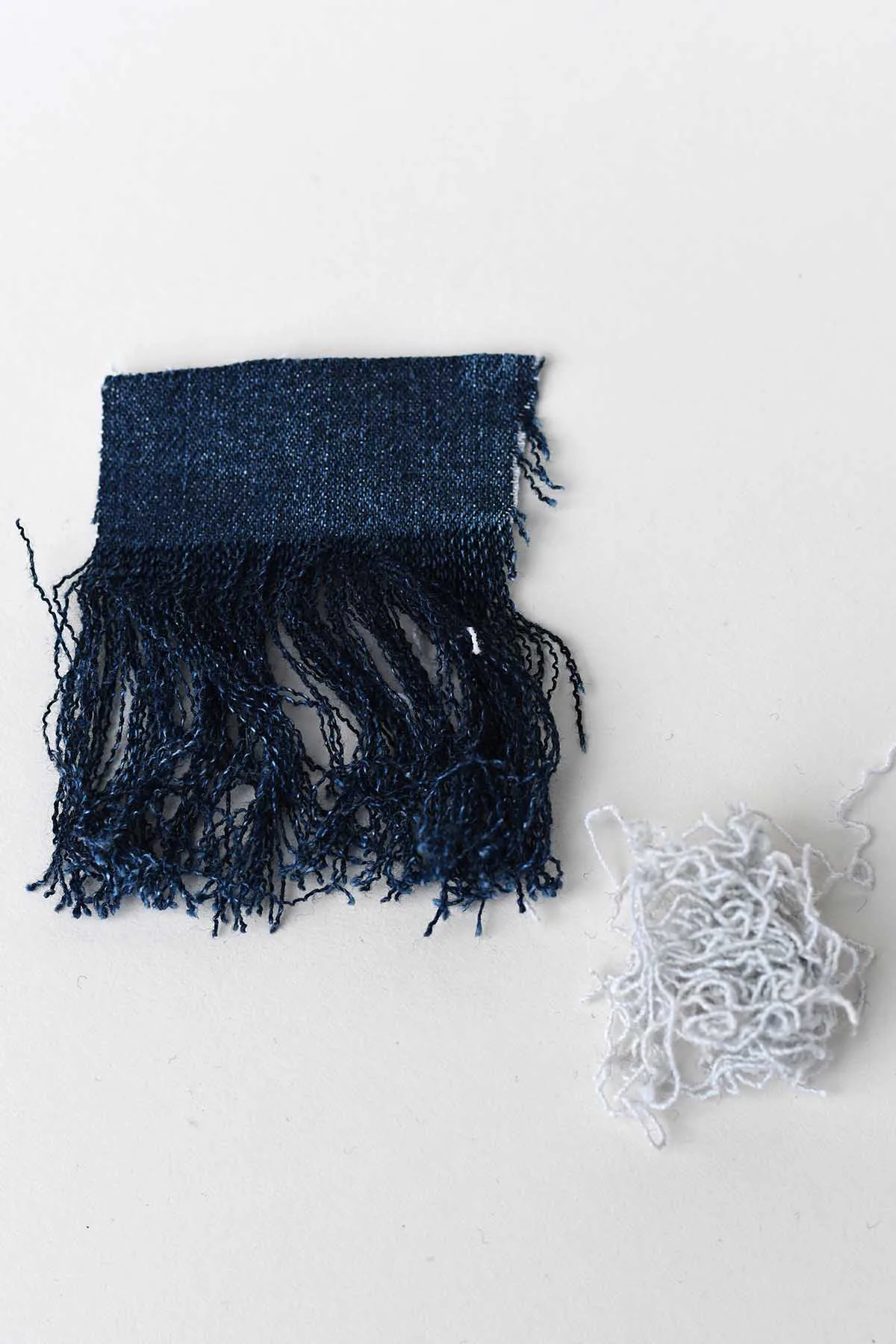 frayed scrap of denim and a pile of white threads that have been removed.
