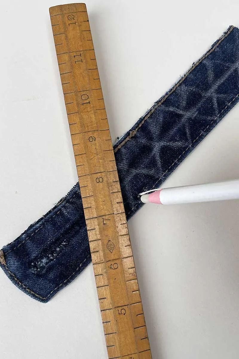 Marking a diamond pattern onto a denim waistband with a white chalk pencil and ruler