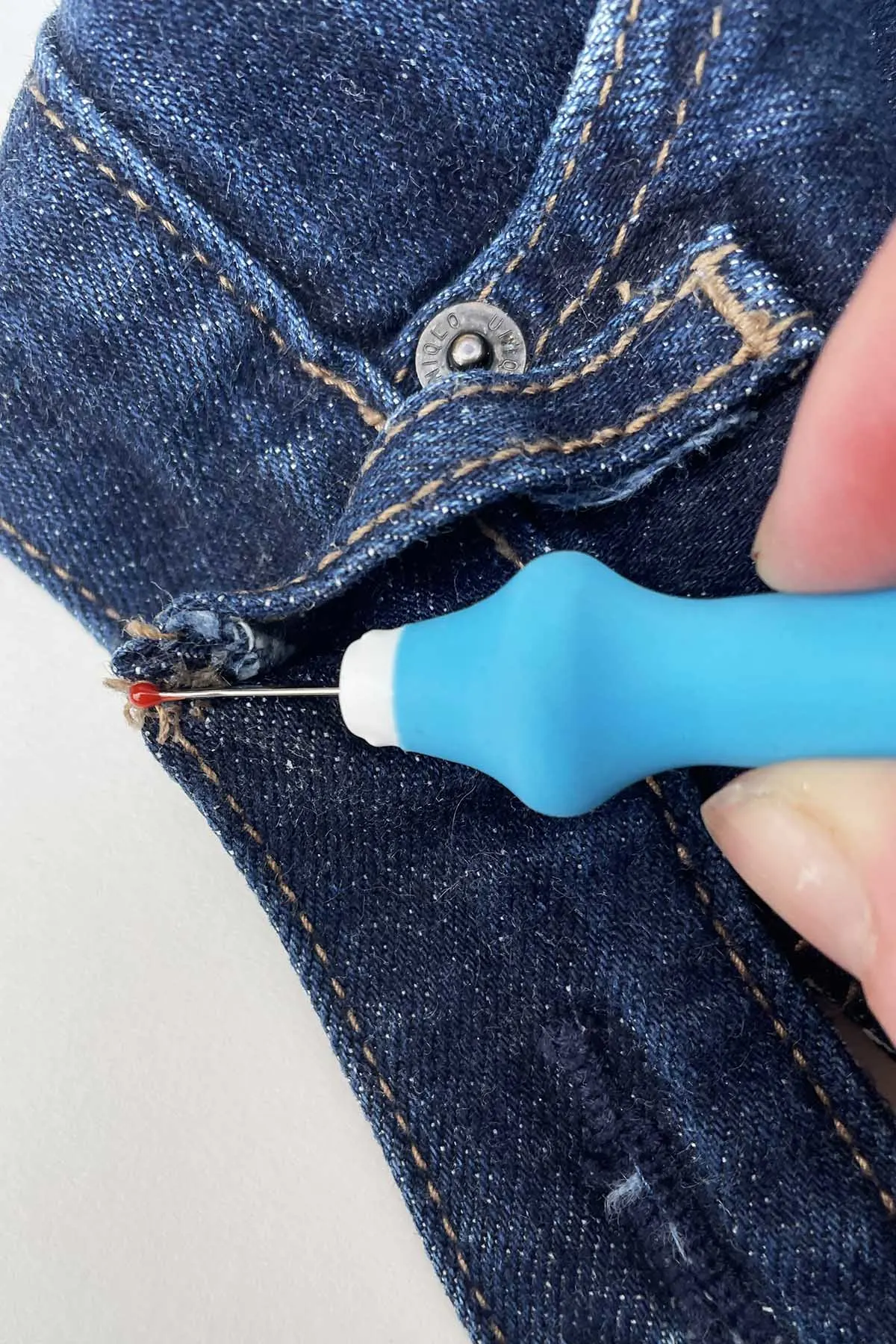Using a seam ripper to remove a belt loop from a jeans waistband