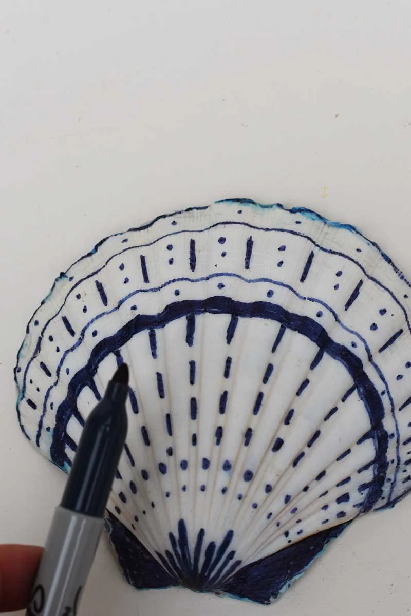 Decorating the back of a scallop shell with a blue  Sharpie pen