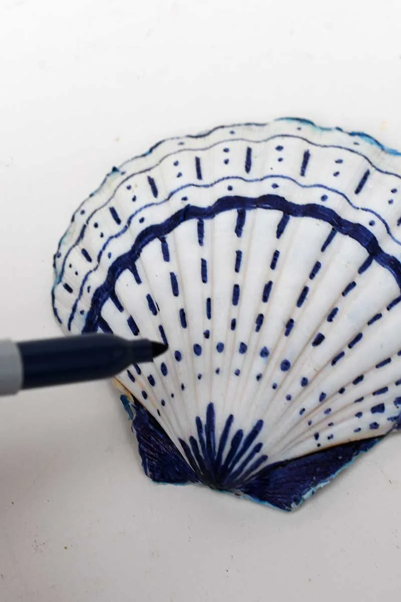 Decorating the back of a scallop shell with a blue Sharpie pen