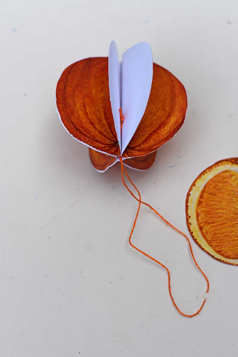 adding twine to center of the paper fruit ornament