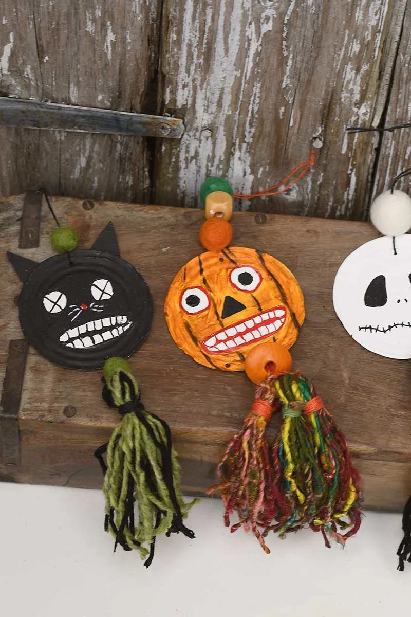 Upcycled tin can halloween decorations black cat, scary pumpkin and Jack Skellington all made from upcycled tin can lids and stitting on a box