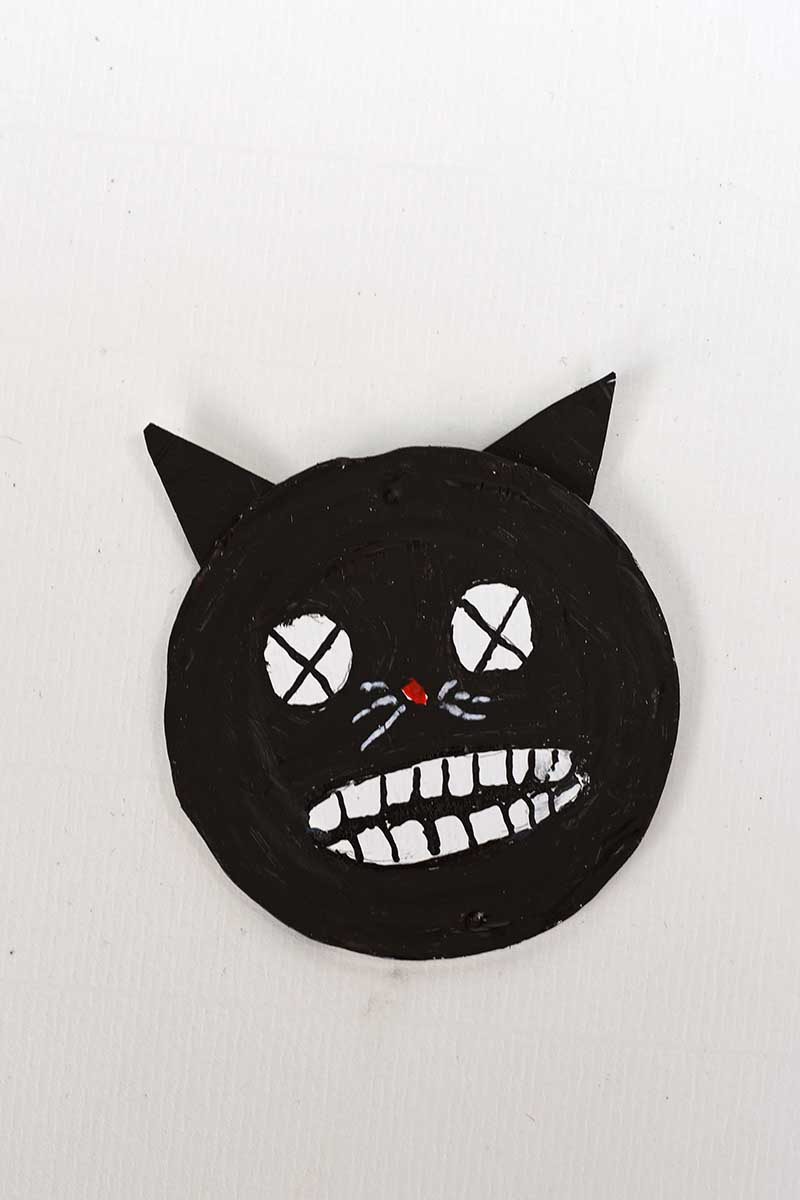 adding ears to the spooky black cat face on tin can lid for Halloween upcycled craft