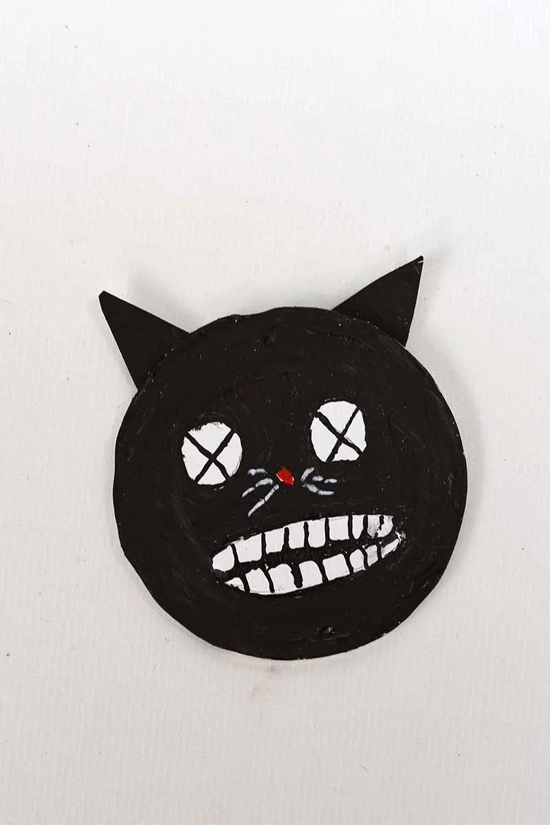 adding ears to the spooky black cat face on tin can lid for Halloween upcycled craft