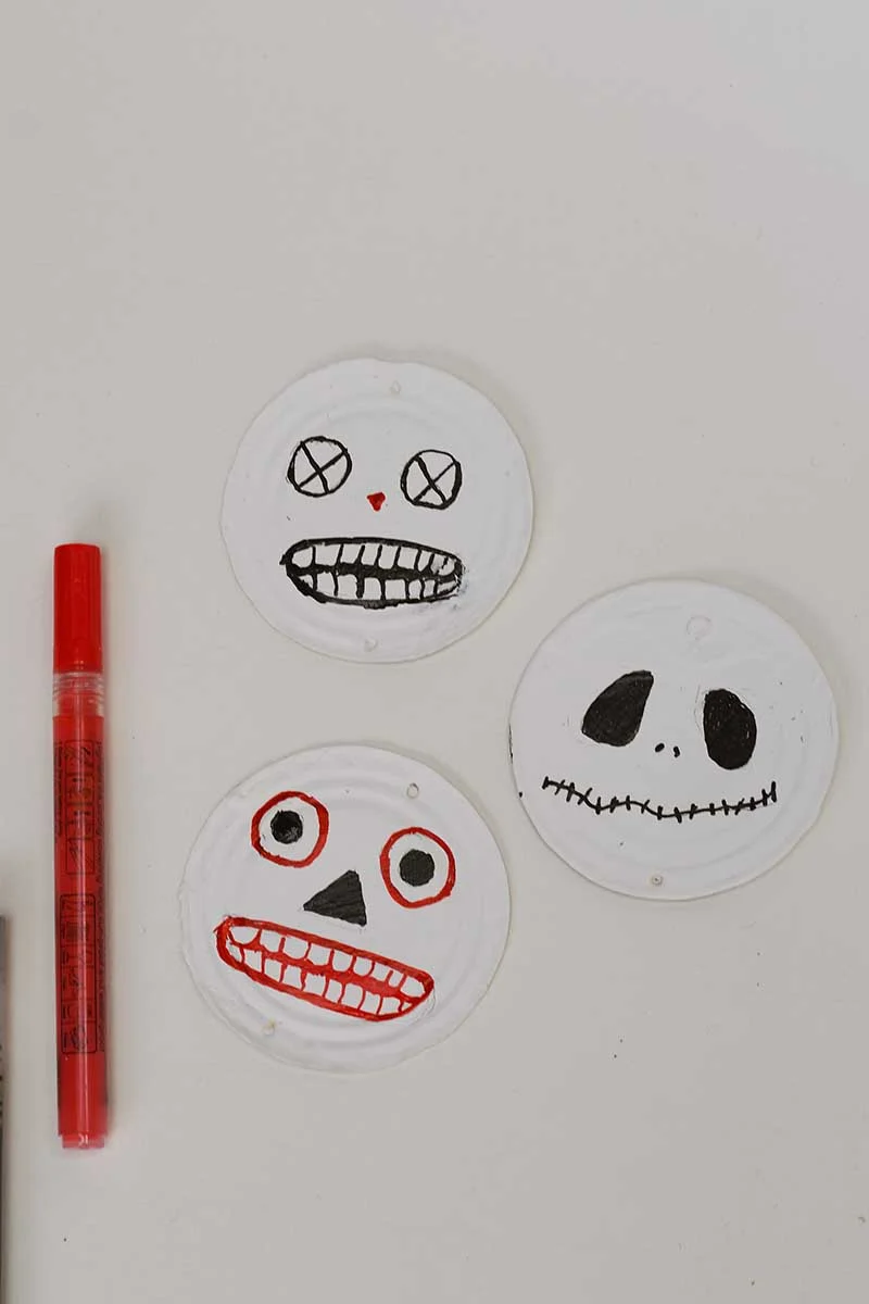 Painting the halloween face details on painted tin can lids with acyrlic paint pens for a retro halloween decoration