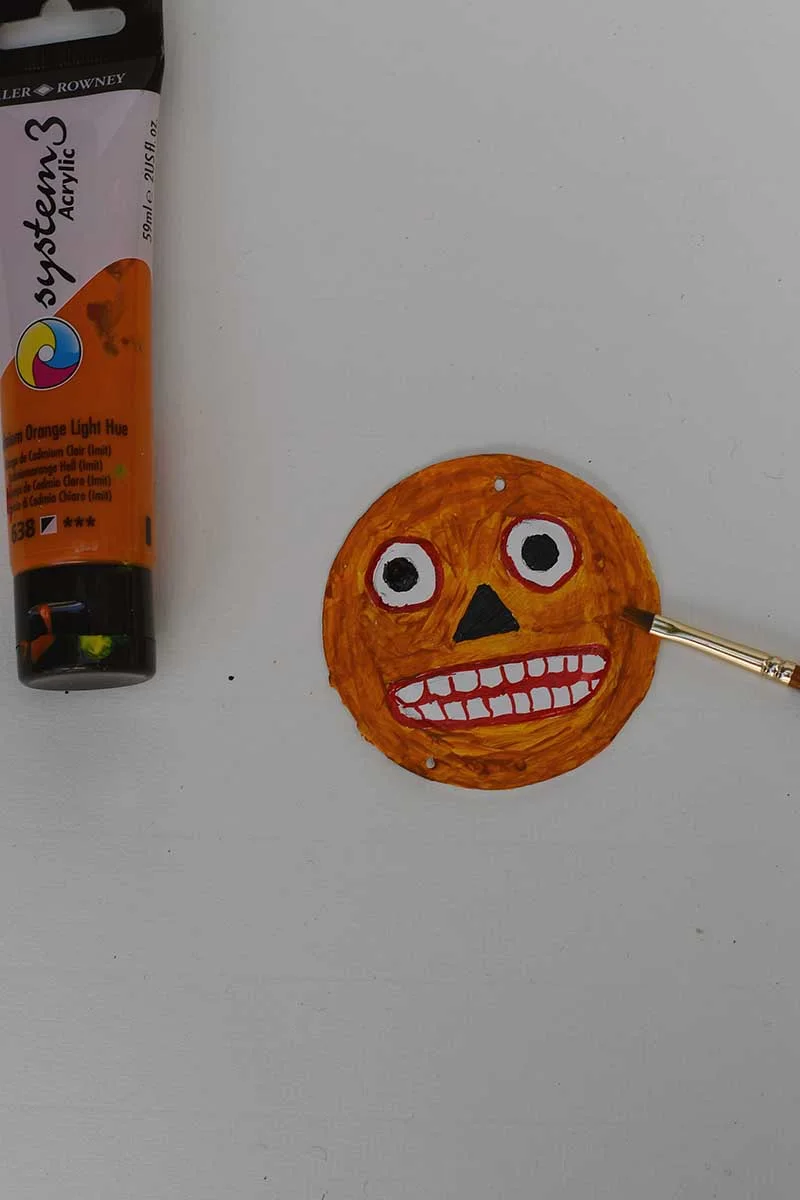 Painting the spooky Halloween pumpkin face on the tin lid orange