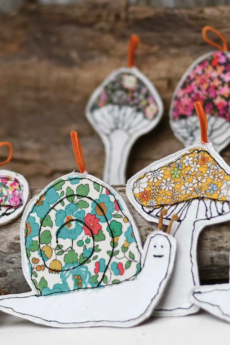 snail and mushroom scrap fabric free embroidery ornaments on a bark background.