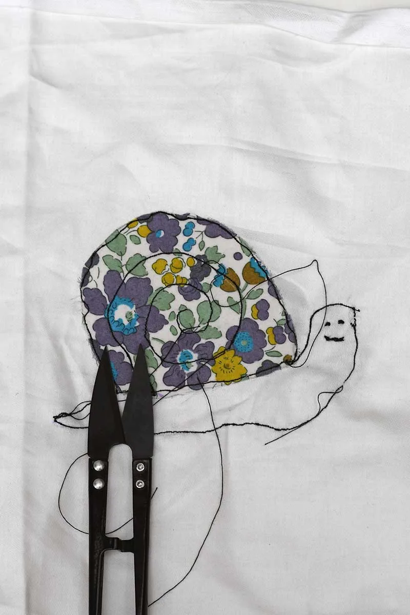 Sewing a face on to the free motion embroidered snails with hand embroidery