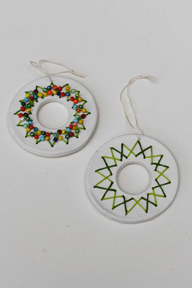 two embroidered clay wreath ornaments, one with beads and the other plain.