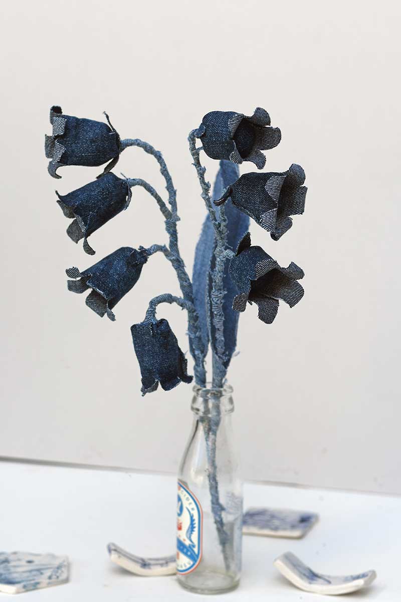 Denim bluebell sprigs of upcycled fabric flowers in a small glass bottle.
