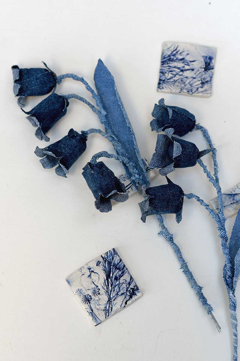 two sprigs of denim bluebell flowers laying flat with blue tiles.