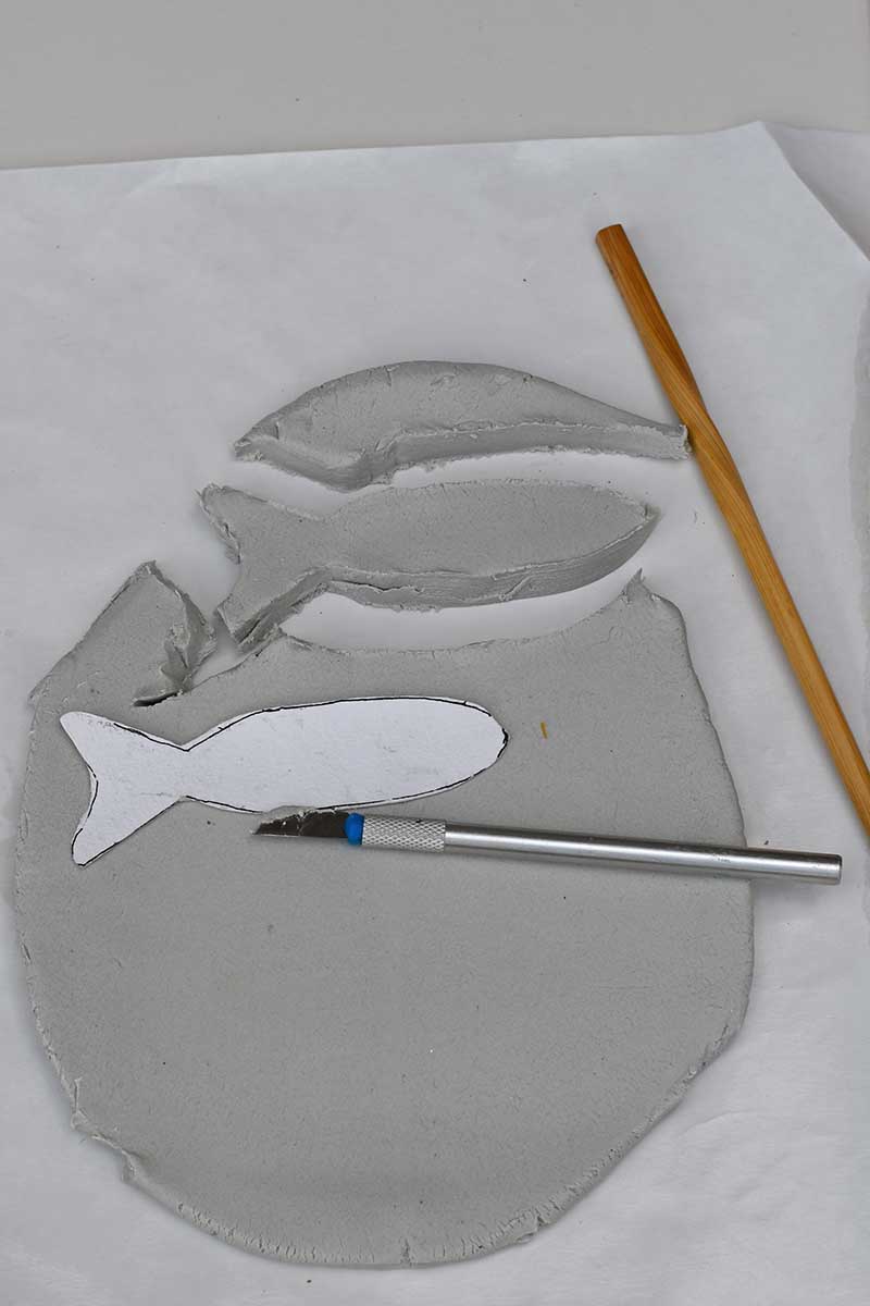 cutting out fish shapes on clay using template
